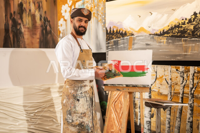 اليوم الوطني العماني 18 نوفمبر، ورشة عمل فنية، رسام عربي خليجي عماني يرتدي الدشداشة والعمامة مع مريلة الرسم يقوم برسم علم سلطنة عمان، إحياء ذكرى تأسيس الدولة 1965، ممارسة الهوايات المفضلة والفنون اليدوية، مفهوم الموهبة و الإبداع وحب الوطن والانتماء إليه
