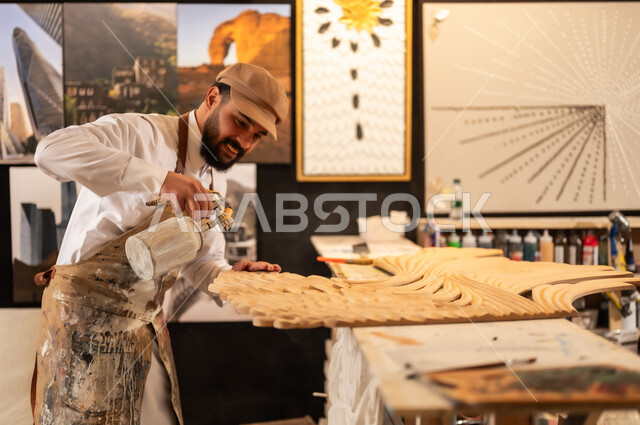 Traditional folk crafts and professions, an exhibition of talents, fine arts and handicrafts, a Saudi Arabian Gulf Arab sculptor wearing traditional thobe and apron spraying sculptures and coloring wood in the workshop, sculptures, decorations and handmade artworks
