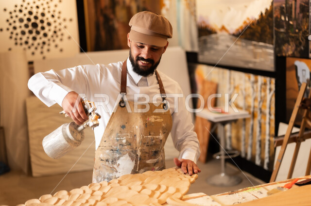 Traditional folk crafts and professions, an exhibition of talents, fine arts and handicrafts, a Saudi Arabian Gulf Arab sculptor wearing traditional thobe and apron spraying sculptures and coloring wood in the workshop, sculptures, decorations and handmade artworks