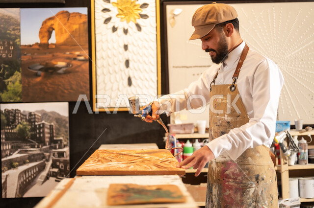 Traditional folk crafts and professions, an exhibition of talents, fine arts and handicrafts, a Saudi Arabian Gulf Arab sculptor wearing traditional thobe and apron spraying sculptures and coloring wood in the workshop, sculptures, decorations and handmade artworks