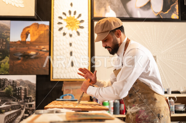 Decorations, sculptures, and handicrafts, traditional folk crafts and professions, an exhibition of talents, fine arts, and handicrafts, a Saudi Arabian Gulf sculptor wearing a traditional thobe and apron, carving and painting on wood in the workshop