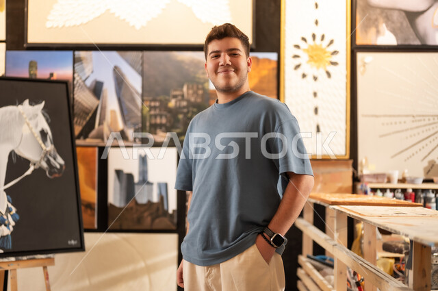 Visiting the art gallery, passion for drawing talent, a young Saudi Arabian Gulf man wearing casual clothes standing with gestures of pleasure and happiness, hanging murals, interest in handicrafts