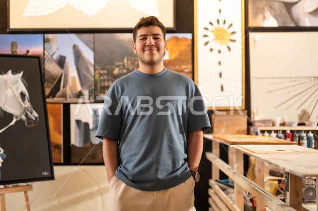 Visiting the art gallery, passion for drawing talent, a young Saudi Arabian Gulf man wearing casual clothes standing with gestures of pleasure and happiness, hanging murals, interest in handicrafts