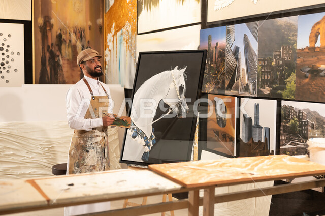 Passion for practicing favorite hobbies and handicrafts, expressions and gestures of integration and pleasure, using a brush to draw on the canvas, the concept of talent and creativity, an art workshop, a Saudi Arabian Gulf Arab painter wearing traditional dress and a painting apron preparing to draw something