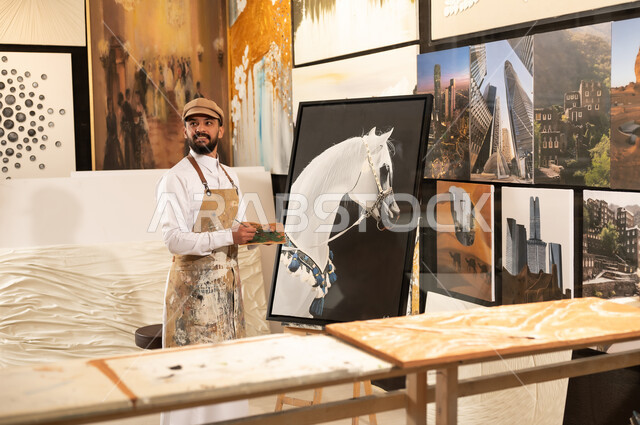 رسام عربي خليجي سعودي يرتدي الثوب التقليدي ومريلة الرسم يستعد لرسم شيء ...