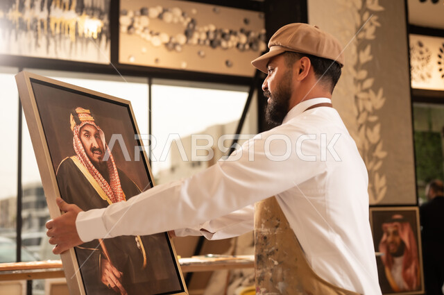 الموهبة و الإبداع في الفنون اليدوية، تعابير السرور والسعادة، مفهوم الحب والانتماء للوطن, ورشة عمل فنية سعودية, رسام عربي خليجي سعودي يرتدي الثوب التقليدي ومريلة الرسم يقدم فنون الرسم و التلوين لصورة الملك عبد العزيز آل سعود