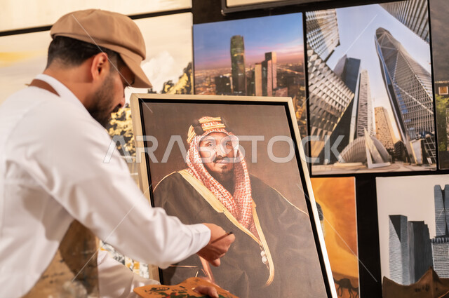 الإبداع والموهبة في الفنون اليدوية، تعابير السرور والسعادة، مفهوم الحب والانتماء للوطن, ورشة عمل فنية سعودية, رسام عربي خليجي سعودي يرتدي الثوب التقليدي ومريلة الرسم يقدم فنون الرسم و التلوين لصورة الملك عبد العزيز آل سعود
