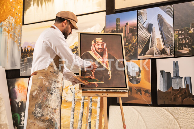الموهبة و الإبداع في الفنون اليدوية، تعابير السرور والسعادة، مفهوم الحب والانتماء للوطن, ورشة عمل فنية سعودية, رسام عربي خليجي سعودي يرتدي الثوب التقليدي ومريلة الرسم يقدم فنون الرسم و التلوين لصورة الملك عبد العزيز آل سعود