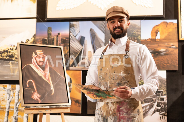 الموهبة و الإبداع في الفنون اليدوية، تعابير السرور والسعادة، مفهوم الحب والانتماء للوطن, ورشة عمل فنية سعودية, رسام عربي خليجي سعودي يرتدي الثوب التقليدي ومريلة الرسم يقدم فنون الرسم و التلوين لصورة الملك عبد العزيز آل سعود