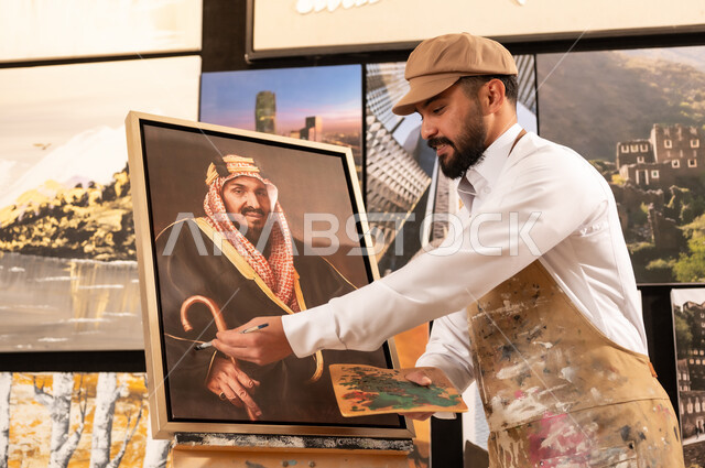 الموهبة و الإبداع في الفنون اليدوية، تعابير السرور والسعادة، مفهوم الحب والانتماء للوطن, ورشة عمل فنية سعودية, رسام عربي خليجي سعودي يرتدي الثوب التقليدي ومريلة الرسم يقدم فنون الرسم و التلوين لصورة الملك عبد العزيز آل سعود