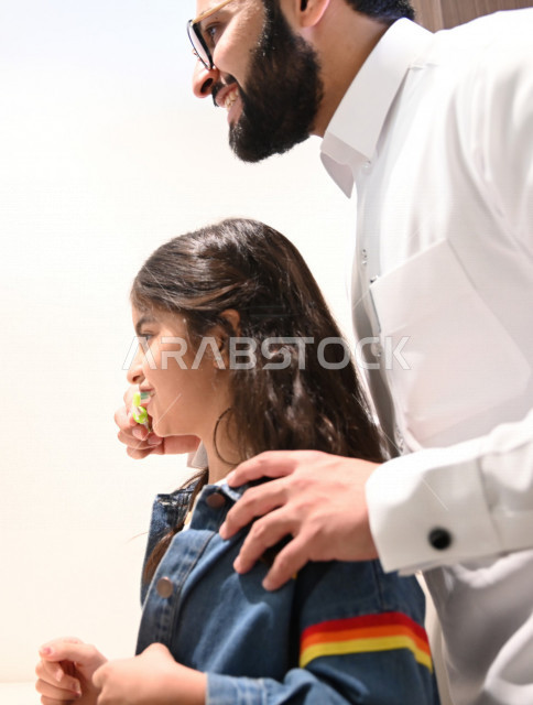 رجل عربي خليجي سعودي يساعد ابنته في تنظيف اسنانها والعناية بها ،تجنب تسوس الاسنان وامراض اللثة ، النظافة الشخصية والاهتمام بالنفس ، الرعاية الصحية للاطفال