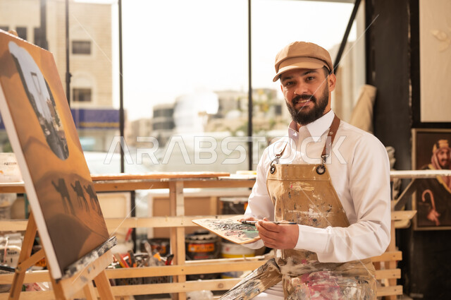معرض الرسومات و اللوحات التشكيلية في العاصمة السعودية, مفهوم الموهبة و الإبداع، ممارسة هواية الفنون اليدوية, الشغف برسم الحيوانات, رسام عربي خليجي سعودي يرتدي الثوب التقليدي ومريلة الرسم  يقوم برسم جمال في الصحراء ومعالم مدينة الرياض