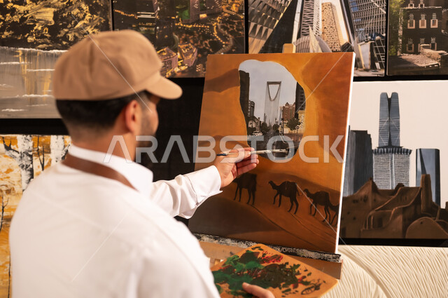 معرض الرسومات و اللوحات التشكيلية في العاصمة السعودية, مفهوم الموهبة و الإبداع، ممارسة هواية الفنون اليدوية, الشغف برسم الحيوانات, رسام عربي خليجي سعودي يرتدي الثوب التقليدي ومريلة الرسم  يقوم برسم جمال في الصحراء ومعالم مدينة الرياض