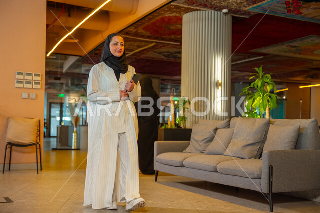 Managing daily work tasks, office jobs and professions, comfortable work environment in Saudi companies, a Saudi Arabian Gulf businesswoman wearing a hijab and abaya holding papers in her hand walking around the company headquarters