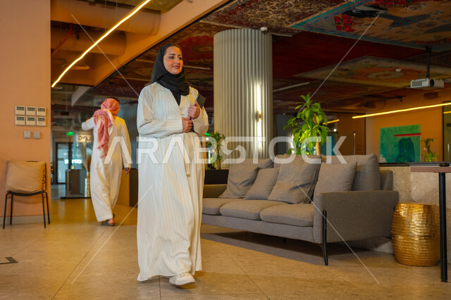 Managing daily work tasks, office jobs and professions, comfortable work environment in Saudi companies, a Saudi Arabian Gulf businesswoman wearing a hijab and abaya holding papers in her hand walking around the company headquarters