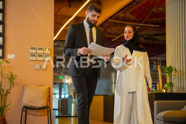 بيئة العمل المريحة في الشركات السعودية, الحوار والنقاش بين الزملاء, تبادل الخبرات والاراء والمعلومات, موظفان عربيان خليجيان سعوديان يتناقشان ويتجولان في مقر الشركة، الاستعداد لحضور اجتماع صباحي