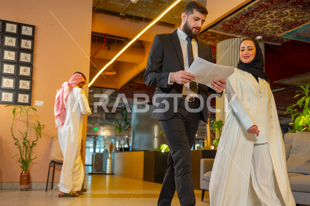 بيئة العمل المريحة في الشركات السعودية, الحوار والنقاش بين الزملاء, تبادل الخبرات والاراء والمعلومات, موظفان عربيان خليجيان سعوديان يتناقشان ويتجولان في مقر الشركة، الاستعداد لحضور اجتماع صباحي