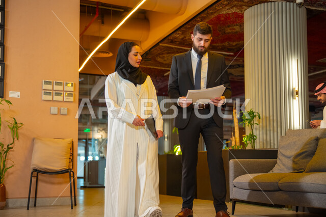 Comfortable work environment in Saudi companies, dialogue and discussion between colleagues, exchange of experiences, opinions and information, two Saudi Gulf Arab employees discussing and touring the company headquarters, preparing to attend a morning meeting