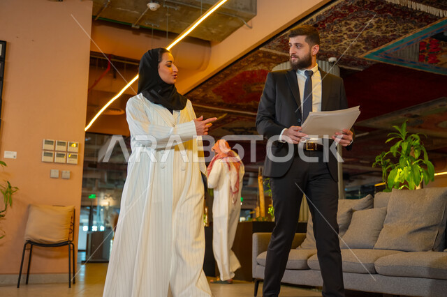 بيئة العمل المريحة في الشركات السعودية, الحوار والنقاش بين الزملاء, تبادل الخبرات والاراء والمعلومات, موظفان عربيان خليجيان سعوديان يتناقشان ويتجولان في مقر الشركة، الاستعداد لحضور اجتماع صباحي