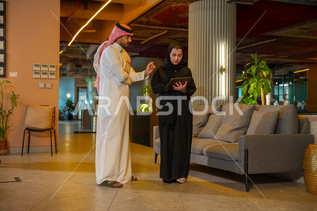 الوحده والعمل الجماعي، تحقيق اهداف الشركة، تطوير العمل وحل المشكلات، مهن ووظائف سعودية مكتبية، تبادل الاراء والخبرات، اجتماع رجل وسيدة اعمال عربيان سعوديان خليجيان يتجولان في مقر الشركة، ادارة العمل باستخدام التابليت، مناقشة وتوزيع مهام العمل، بيئة العمل السعودي