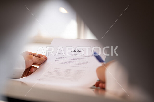 رجل عربي خليجي سعودي يمسك بيده ورقة عرض مالي، قراءة بنود العرض، التحقق والتدقيق في العرض المالي، الموافقة على العرض المالي