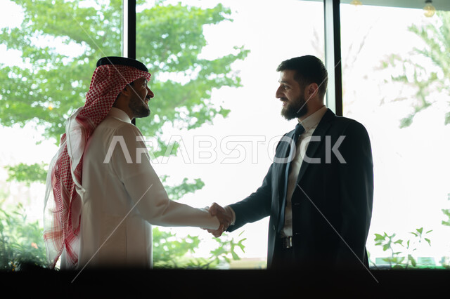 اجراء مقابلة توظيف واختبار، تبادل المعلومات والخبرات، رجل اعمال عربي سعودي خليجي يرتدي الثوب التقليدي والشماغ يصافح شاب يرتدي البدلة الرسمية، اتفاقية عمل لمشروع جديد، الموافقة على شروط العمل، توقيع عقود العمل