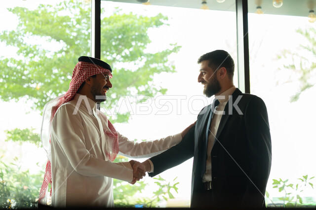 اجراء مقابلة توظيف واختبار، تبادل المعلومات والخبرات، رجل اعمال عربي سعودي خليجي يرتدي الثوب التقليدي والشماغ يصافح شاب يرتدي البدلة الرسمية، اتفاقية عمل لمشروع جديد، الموافقة على شروط العمل، توقيع عقود العمل