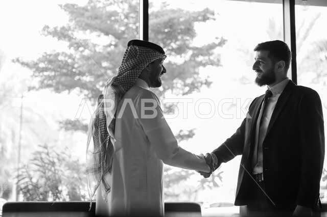 اجراء مقابلة توظيف واختبار، تبادل المعلومات والخبرات، رجل اعمال عربي سعودي خليجي يرتدي الثوب التقليدي والشماغ يصافح شاب يرتدي البدلة الرسمية، اتفاقية عمل لمشروع جديد، الموافقة على شروط العمل، توقيع عقود العمل