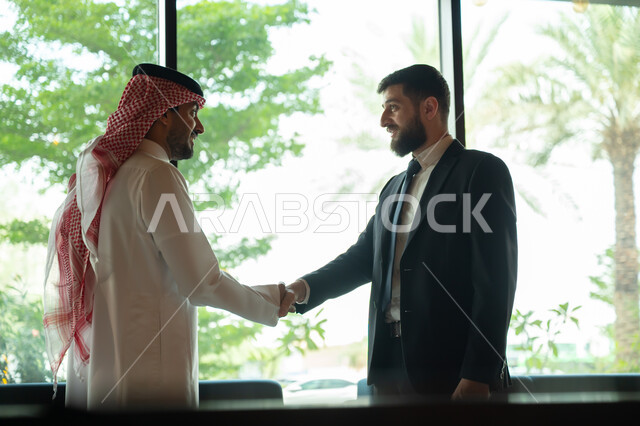 اجراء مقابلة توظيف واختبار، تبادل المعلومات والخبرات، رجل اعمال عربي سعودي خليجي يرتدي الثوب التقليدي والشماغ يصافح شاب يرتدي البدلة الرسمية، اتفاقية عمل لمشروع جديد، الموافقة على شروط العمل، توقيع عقود العمل