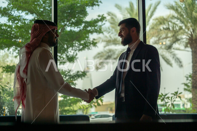 اجراء مقابلة توظيف واختبار، تبادل المعلومات والخبرات، رجل اعمال عربي سعودي خليجي يرتدي الثوب التقليدي والشماغ يصافح شاب يرتدي البدلة الرسمية، اتفاقية عمل لمشروع جديد، الموافقة على شروط العمل، توقيع عقود العمل