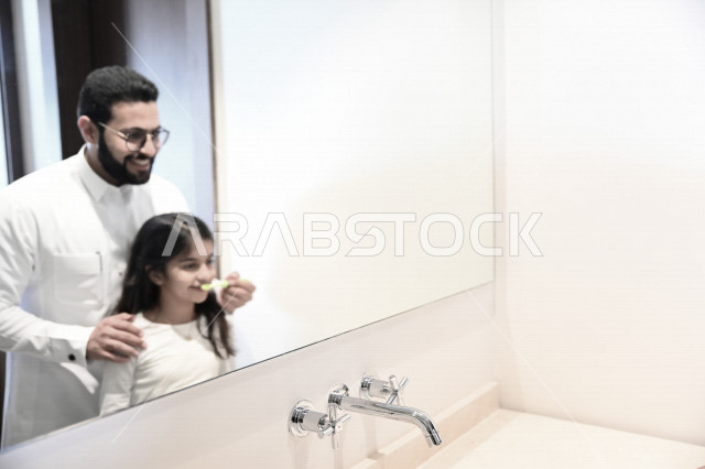 رجل عربي خليجي سعودي يساعد ابنته في تنظيف اسنانها والعناية بها ،تجنب تسوس الاسنان وامراض اللثة ، النظافة الشخصية والاهتمام بالنفس ، الرعاية الصحية للاطفال