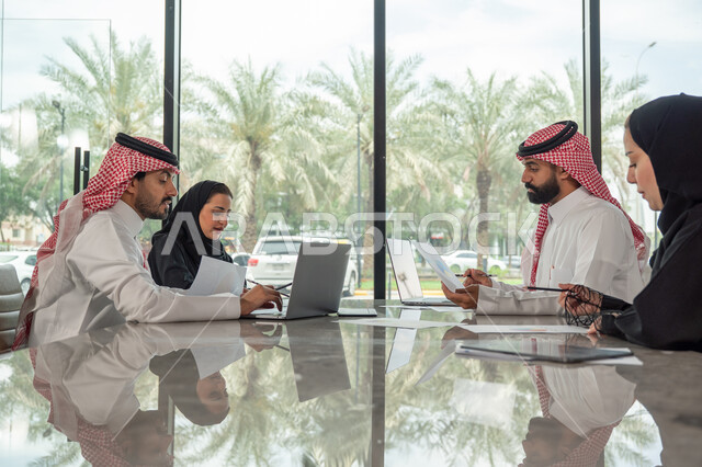 Explaining and analyzing graphs, integrating modern technical devices into office work, studying statistical data sheets, developing projects and investments, managing and dividing tasks, an Arab Gulf Saudi team conducting a business meeting in the conference room at the company's headquarters