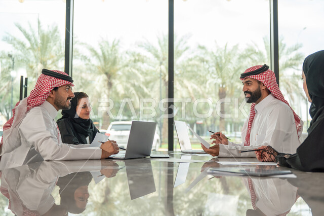 Explaining and analyzing graphs, integrating modern technical devices into office work, studying statistical data sheets, developing projects and investments, managing and dividing tasks, an Arab Gulf Saudi team conducting a business meeting in the conference room at the company's headquarters
