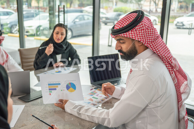 شرح و تحليل الرسوم البيانية, دمج الأجهزة التقنية الحديثة بالأعمال المكتبية، دراسة أوراق البيانات الإحصائية, تطوير المشاريع و الاستثمارات, إدارة و تقسيم المهام، فريق عمل عربي خليجي سعودي يقوم بإجراء اجتماع عمل داخل غرفة الاجتماعات في مقر الشركة