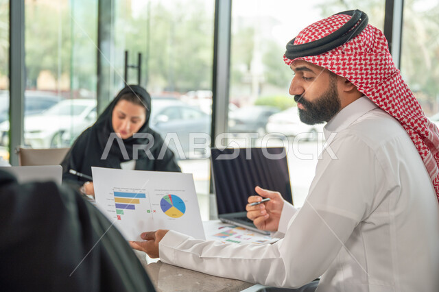 شرح و تحليل الرسوم البيانية, دمج الأجهزة التقنية الحديثة بالأعمال المكتبية، دراسة أوراق البيانات الإحصائية, تطوير المشاريع و الاستثمارات, إدارة و تقسيم المهام، فريق عمل عربي خليجي سعودي يقوم بإجراء اجتماع عمل داخل غرفة الاجتماعات في مقر الشركة