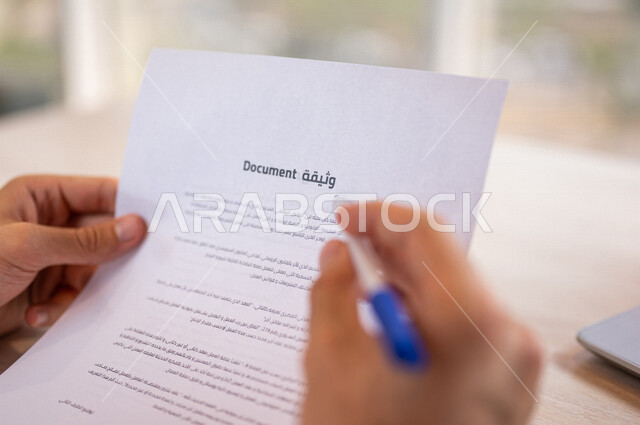 رجل عربي خليجي سعودي يمسك بيده قلم ويقوم بقراءة وثيقة، سكرتير يدير الاعمال الورقية، التحقق والتدقيق في الوثيقة، مفهوم التوظيف والعمل، أعمال مكتبية