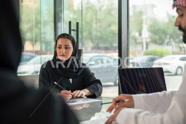 شرح و تحليل الرسوم البيانية, دمج الأجهزة التقنية الحديثة بالأعمال المكتبية، دراسة أوراق البيانات الإحصائية, تطوير المشاريع و الاستثمارات, إدارة و تقسيم المهام، فريق عمل عربي خليجي سعودي يقوم بإجراء اجتماع عمل داخل غرفة الاجتماعات في مقر الشركة
