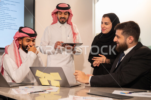 دمج الأجهزة التقنية الحديثة بالأعمال المكتبية، دراسة أوراق البيانات الإحصائية, تطوير المشاريع و الاستثمارات, إدارة و تقسيم المهام، فريق عمل عربي خليجي سعودي يقوم بإجراء اجتماع عمل داخل غرفة الاجتماعات في مقر الشركة، شرح و تحليل الرسوم البيانية