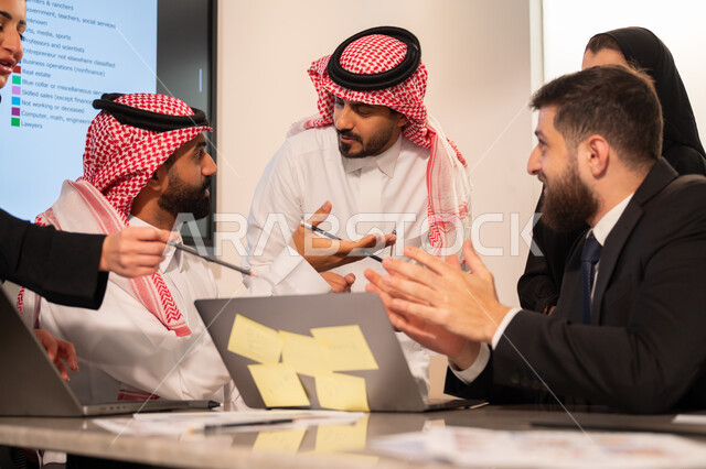 دمج الأجهزة التقنية الحديثة بالأعمال المكتبية، دراسة أوراق البيانات الإحصائية, تطوير المشاريع و الاستثمارات, إدارة و تقسيم المهام، فريق عمل عربي خليجي سعودي يقوم بإجراء اجتماع عمل داخل غرفة الاجتماعات في مقر الشركة، شرح و تحليل الرسوم البيانية