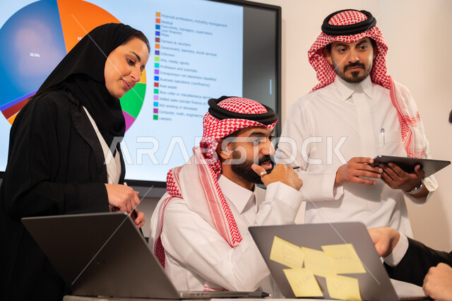 دمج الأجهزة التقنية الحديثة بالأعمال المكتبية، دراسة أوراق البيانات الإحصائية, تطوير المشاريع و الاستثمارات, إدارة و تقسيم المهام، فريق عمل عربي خليجي سعودي يقوم بإجراء اجتماع عمل داخل غرفة الاجتماعات في مقر الشركة، شرح و تحليل الرسوم البيانية