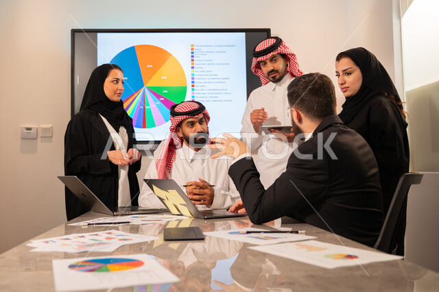 دمج الأجهزة التقنية الحديثة بالأعمال المكتبية، دراسة أوراق البيانات الإحصائية, تطوير المشاريع و الاستثمارات, إدارة و تقسيم المهام، فريق عمل عربي خليجي سعودي يقوم بإجراء اجتماع عمل داخل غرفة الاجتماعات في مقر الشركة، شرح و تحليل الرسوم البيانية