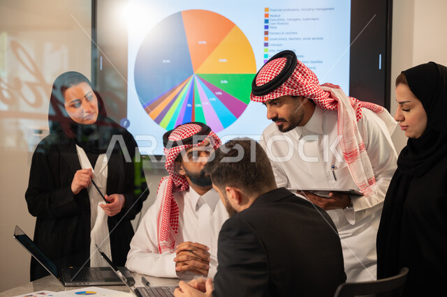 دمج الأجهزة التقنية الحديثة بالأعمال المكتبية، دراسة أوراق البيانات الإحصائية, تطوير المشاريع و الاستثمارات, إدارة و تقسيم المهام، فريق عمل عربي خليجي سعودي يقوم بإجراء اجتماع عمل داخل غرفة الاجتماعات في مقر الشركة، شرح و تحليل الرسوم البيانية