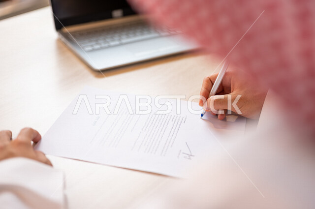 رجل عربي خليجي سعودي يجلس أمام الحاسوب المحمول ويقوم بتوقيع عقد إيجار، قراءة البنود الخاصة بالعقد، التحقق والتدقيق في شروط عقد الايجار، الموافقة على الشروط، التوقيع على العقود
