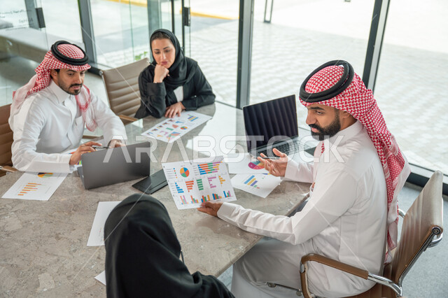 دمج الأجهزة التقنية الحديثة بالأعمال المكتبية، دراسة أوراق البيانات الإحصائية, تطوير المشاريع و الاستثمارات, إدارة و تقسيم المهام، فريق عمل عربي خليجي سعودي يقوم بإجراء اجتماع عمل داخل غرفة الاجتماعات في مقر الشركة، شرح و تحليل الرسوم البيانية
