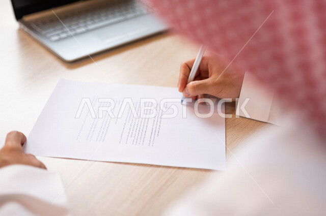 رجل عربي خليجي سعودي يجلس أمام الحاسوب المحمول ويقوم بتوقيع عقد إيجار، قراءة البنود الخاصة بالعقد، التحقق والتدقيق في شروط عقد الايجار، الموافقة على الشروط، التوقيع على العقود