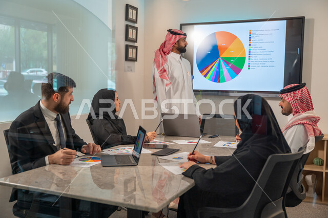  إدارة و تقسيم المهام، فريق عمل عربي خليجي سعودي يقوم بإجراء اجتماع عمل داخل غرفة الاجتماعات في مقر الشركة، شرح و تحليل الرسوم البيانية, دمج الأجهزة التقنية الحديثة بالأعمال المكتبية، دراسة أوراق البيانات الإحصائية, تطوير المشاريع و الاستثمارات