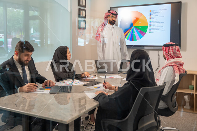  إدارة و تقسيم المهام، فريق عمل عربي خليجي سعودي يقوم بإجراء اجتماع عمل داخل غرفة الاجتماعات في مقر الشركة، شرح و تحليل الرسوم البيانية, دمج الأجهزة التقنية الحديثة بالأعمال المكتبية، دراسة أوراق البيانات الإحصائية, تطوير المشاريع و الاستثمارات