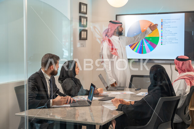  إدارة و تقسيم المهام، فريق عمل عربي خليجي سعودي يقوم بإجراء اجتماع عمل داخل غرفة الاجتماعات في مقر الشركة، شرح و تحليل الرسوم البيانية, دمج الأجهزة التقنية الحديثة بالأعمال المكتبية، دراسة أوراق البيانات الإحصائية, تطوير المشاريع و الاستثمارات