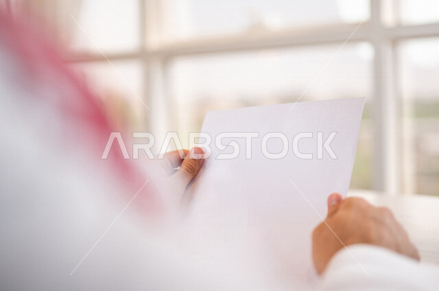 رجل عربي خليجي سعودي يحمل بيده أوراق بيضاء فارغة، سكرتير يدير الأعمال الورقية، اعمال مكتبية
