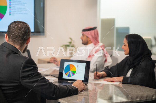  إدارة و تقسيم المهام، فريق عمل عربي خليجي سعودي يقوم بإجراء اجتماع عمل داخل غرفة الاجتماعات في مقر الشركة، شرح و تحليل الرسوم البيانية, دمج الأجهزة التقنية الحديثة بالأعمال المكتبية، دراسة أوراق البيانات الإحصائية, تطوير المشاريع و الاستثمارات